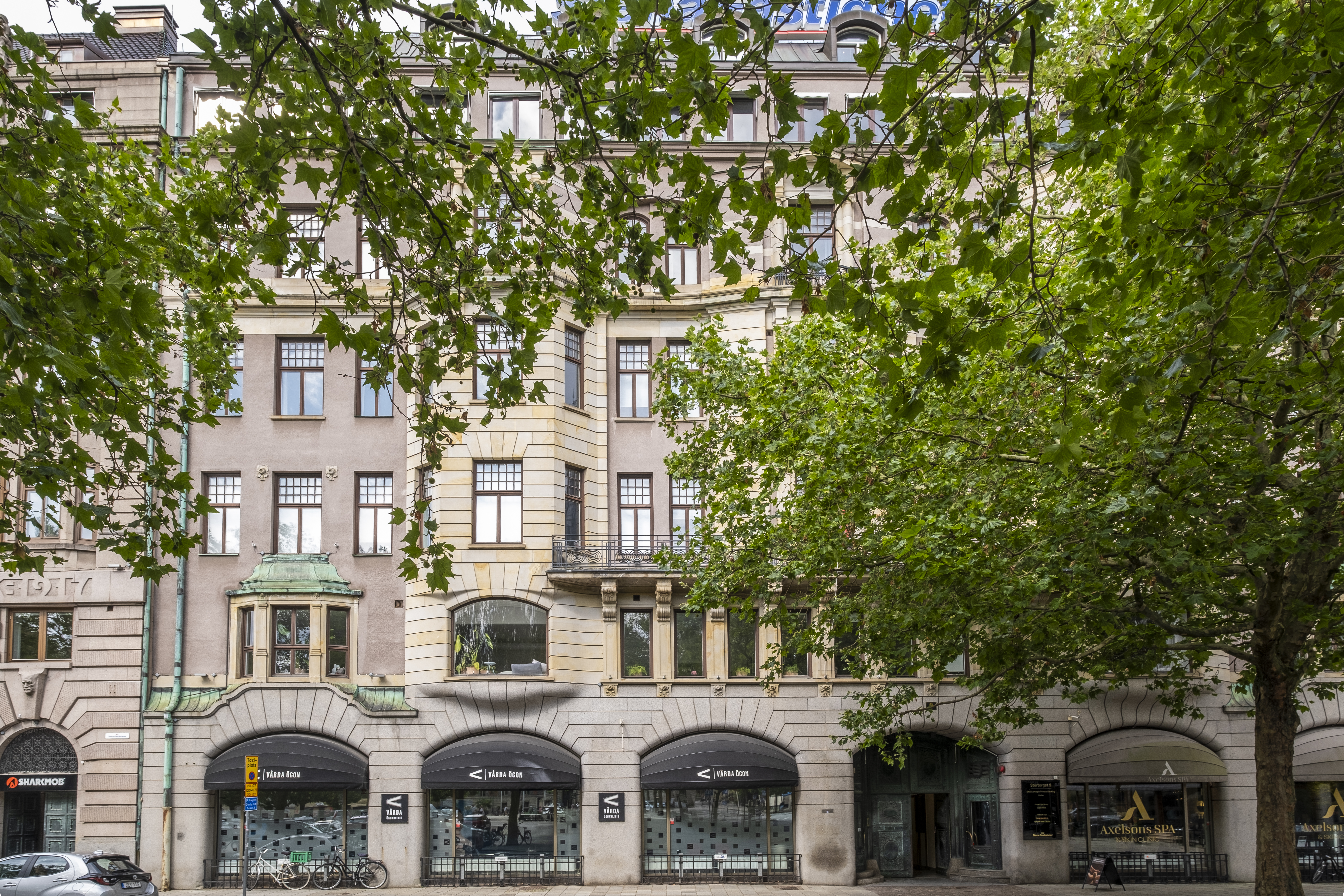 Ett vackert hus med ljus fasad och flera våningar, delvis skymt av grönskande träd och buskar.