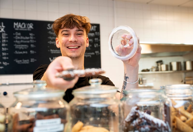 En persom som arbetar på ett café håller i en kaka. 