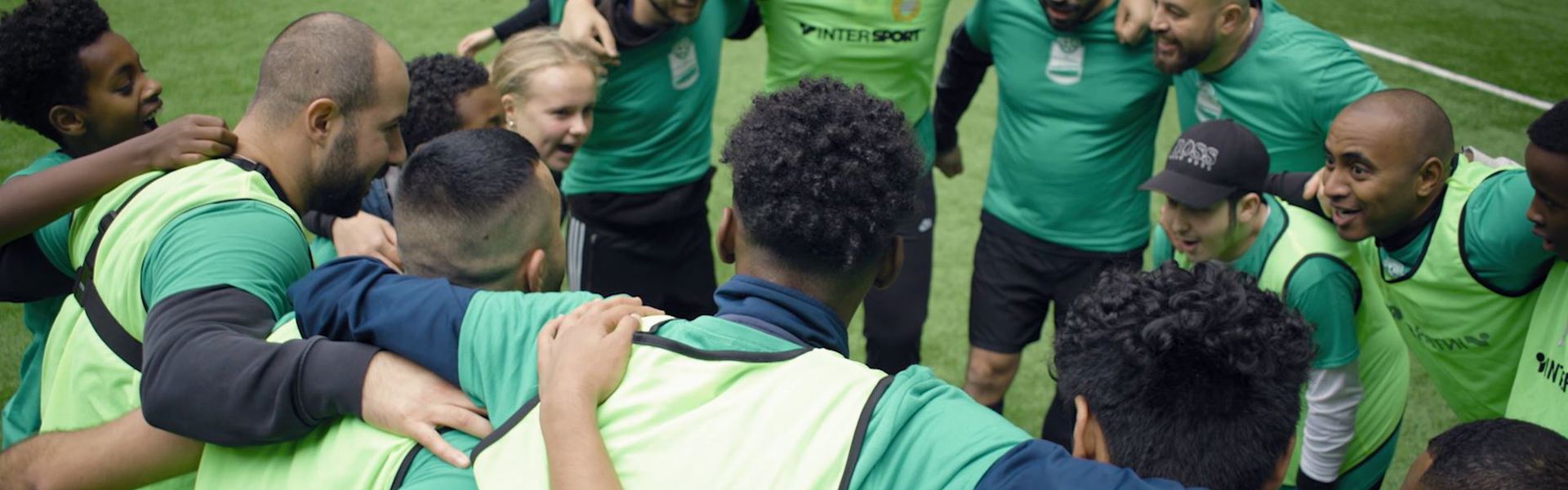 Grupp med ungdomar och vuxna som står i ring med armarna runt om varandra och peppar varandra inför fotbollsmatch