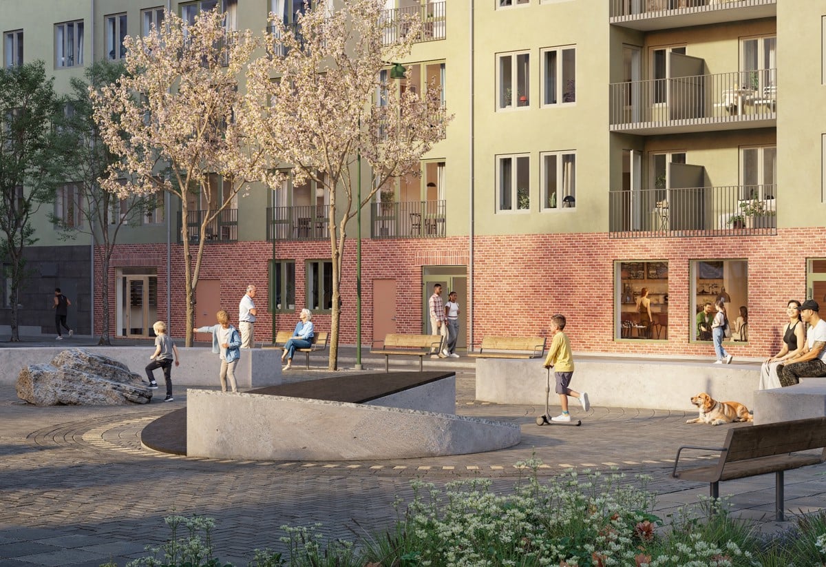 En solig innergård framför ett flerbostadshus med grön fasad och röd tegelsockel, där människor i olika åldrar sitter på bänkar, pratar, leker och promenerar bland träd, planteringar och låga betongmurar.