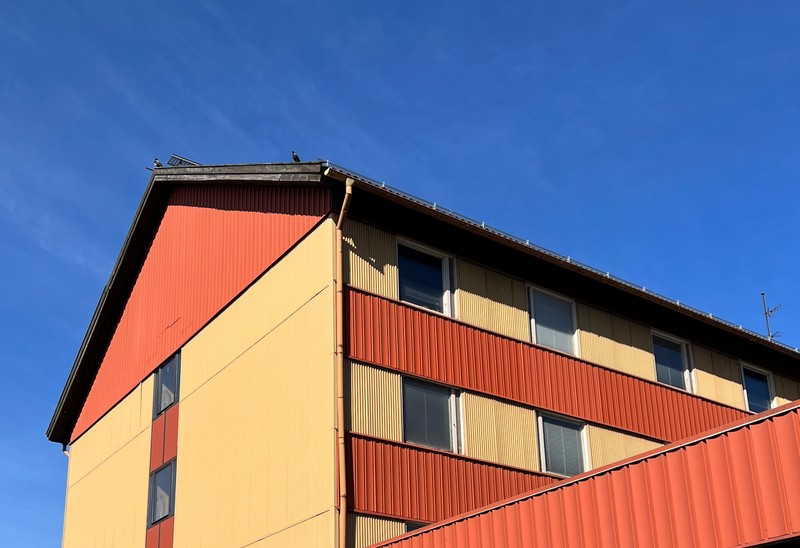 Gul hus-fasad med röda detaljer mot klar blå himmel