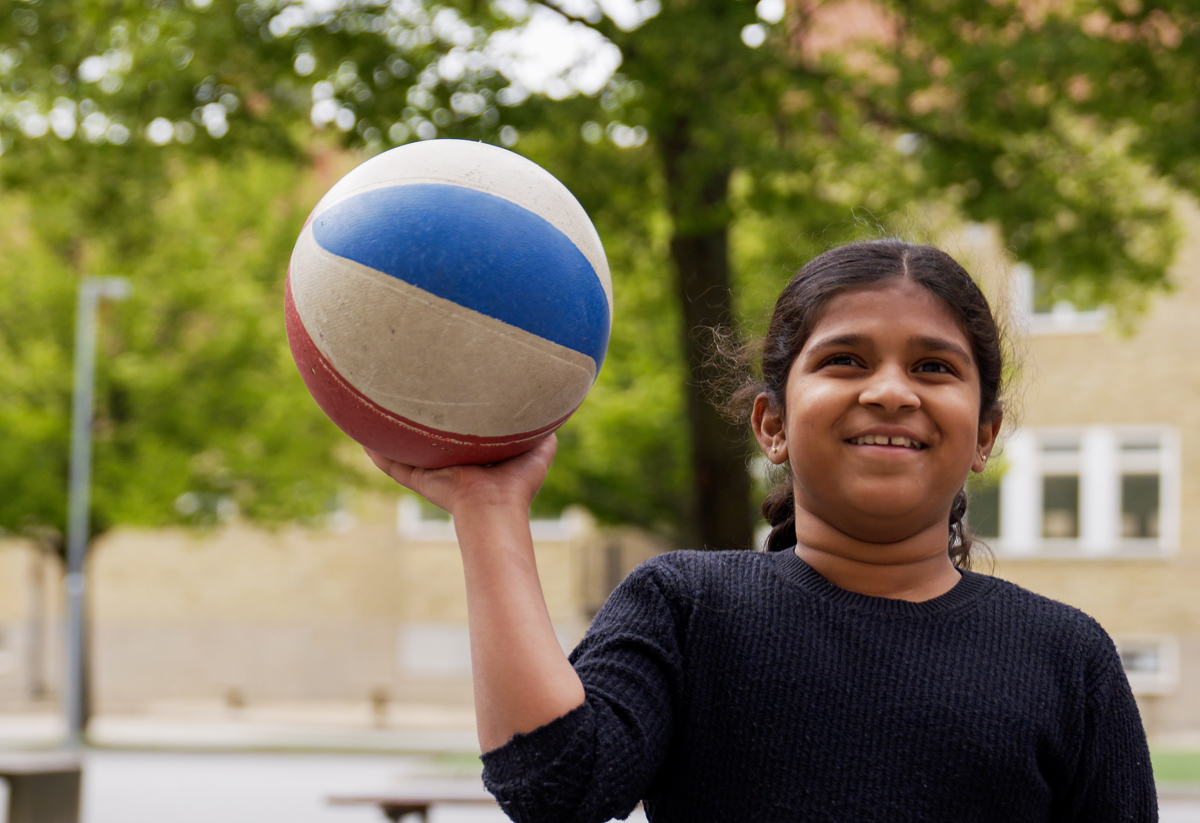 Tjej på sommarskolan som håller en basketboll. 