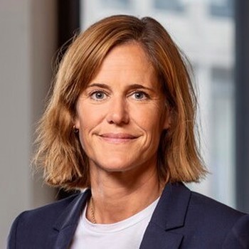 En kvinna, Cecilia Fasth, ler och ser glad ut, med kopparfärgat hår och en mörkblå kavaj. Hon bär en vit t-shirt och tittar i kameran.