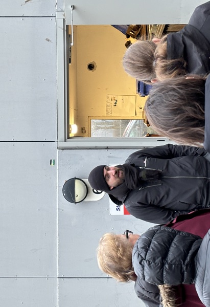 En mörklädd man står utanför ett soprum och pratar med andra människor