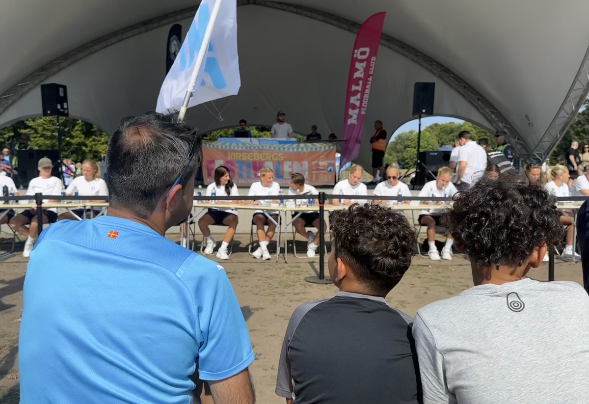 Tre som sitter på en bänk framför Malmö FFs damlag som skriver autografer