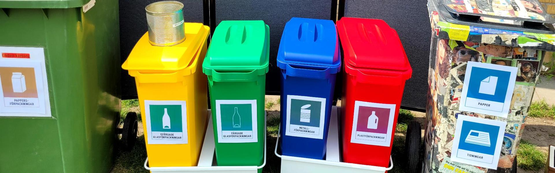 Soptunnor i olika färger med färgglada lappar som sitter på en vägg bakom dom