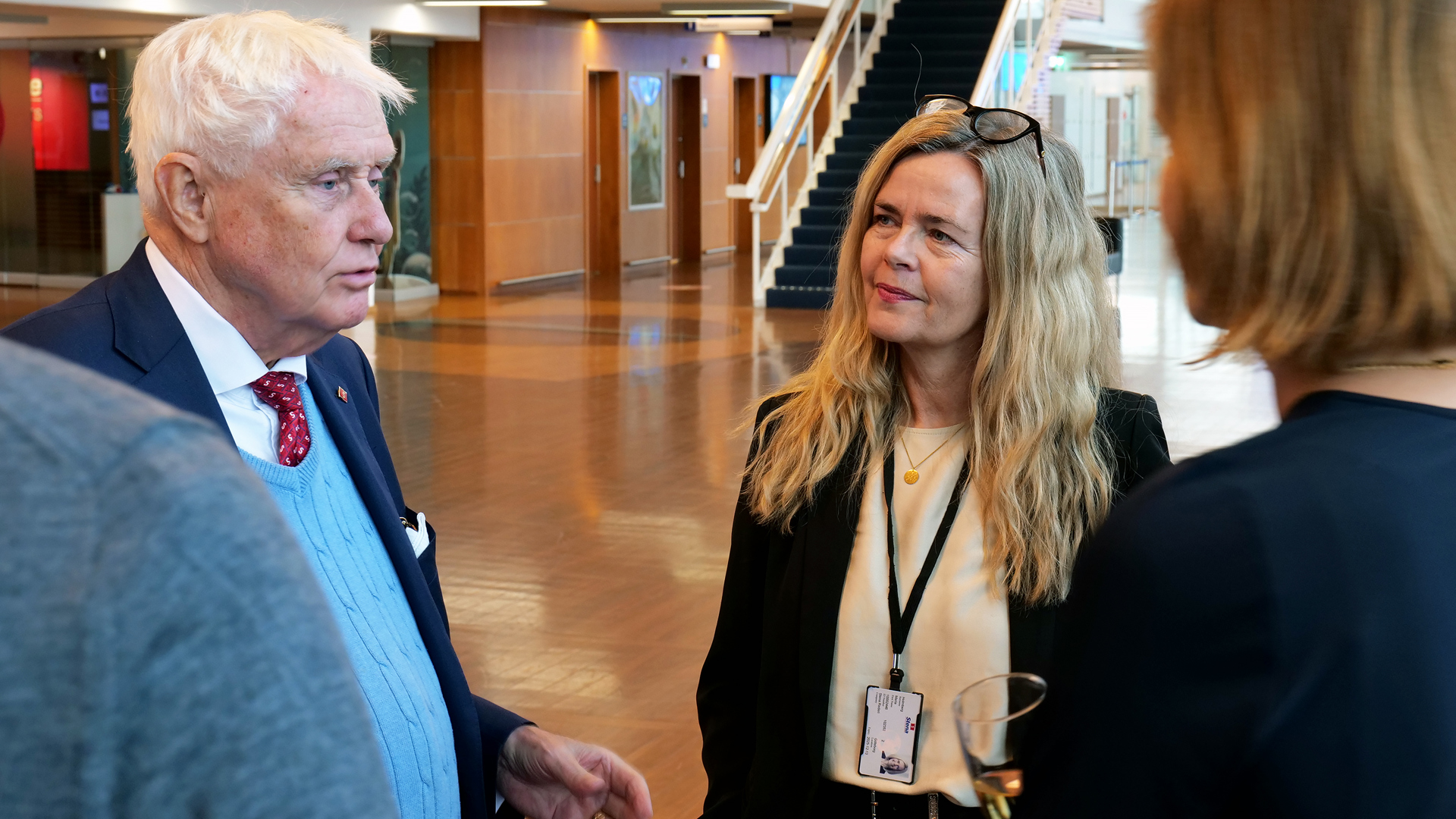Tre personer står och pratar i en utställnings-sal. I bakgrunden syns en stor och luftig lokal och en trappa. 