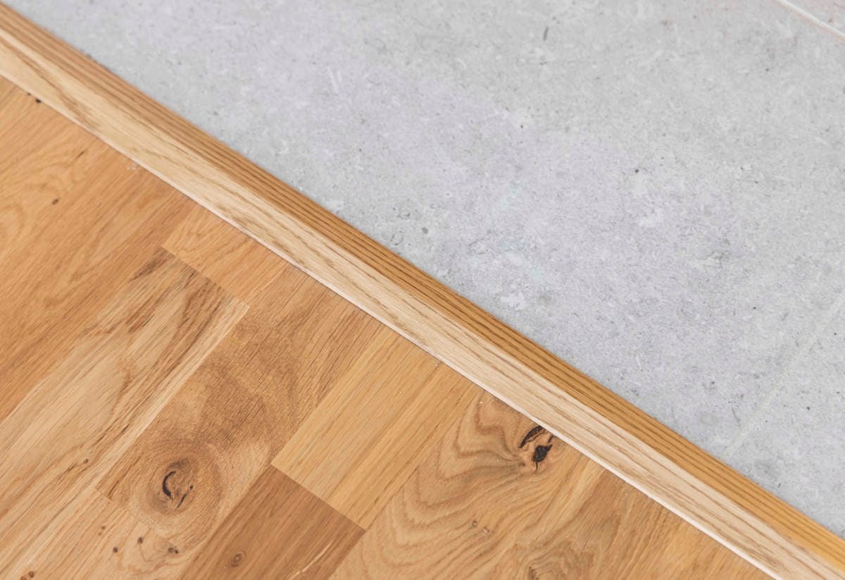 Detaljbild från en plusrenoverad lägenhet med fokus på parkettgolv och klinker i hall
