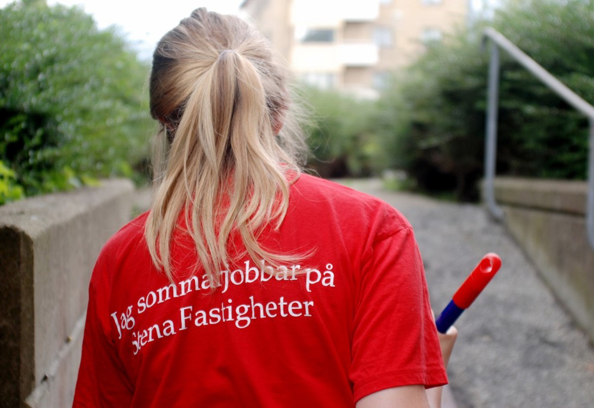 Blond tjej fotad bakifrån. Hon bär en röd t-shirt med texten ´Jag sommarjobbar på Stena Fastigheter` på ryggen. 