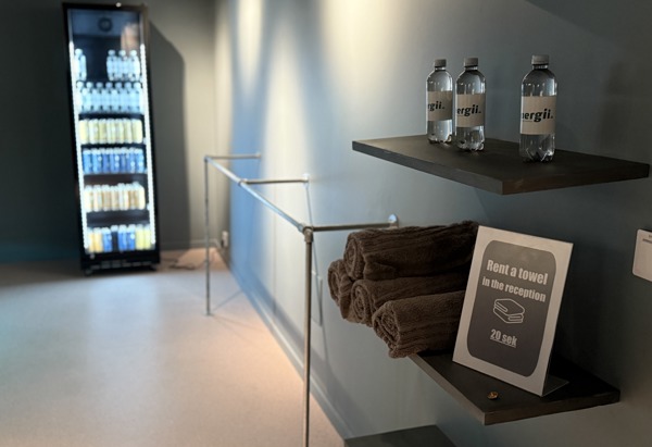 En vägg med en stång. Hyllor med vattenflaskor på och handdukar med en skylt om att man kan hyra en handduk. En kyl med kylda drycker i.