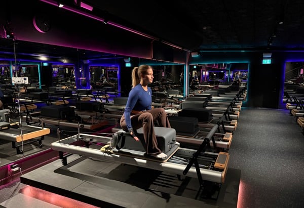 Person som tränar på en pilatesmaskin i ett mörkt rum med svag belysning i olika färger.