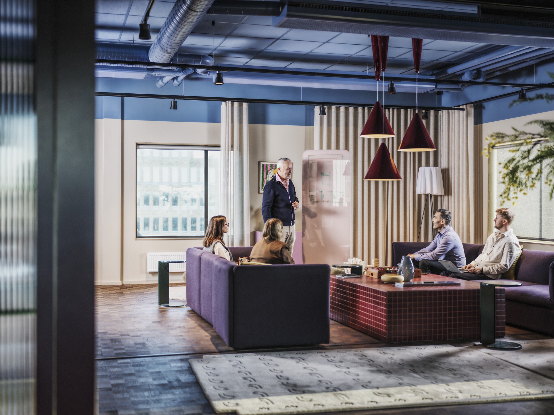 Fem personer i ett stort rymligt mötesrum, en person står upp vid en bildskärm