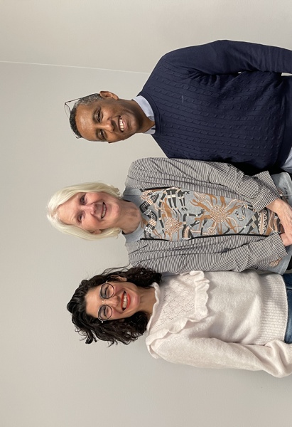 två kvinnor och en man som poserar stående framför kameran.