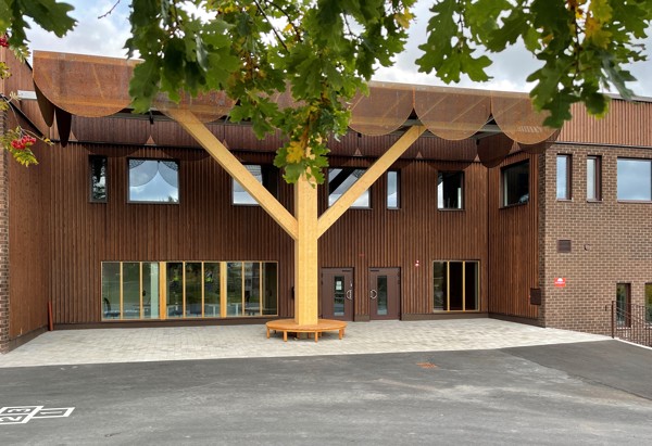 Brun skolbyggnad som syns bakom en ekgren. 
