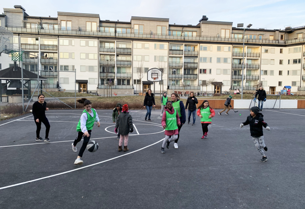 Barn och ungdomar som spelar basket i två lag på en basketplan utomhus.