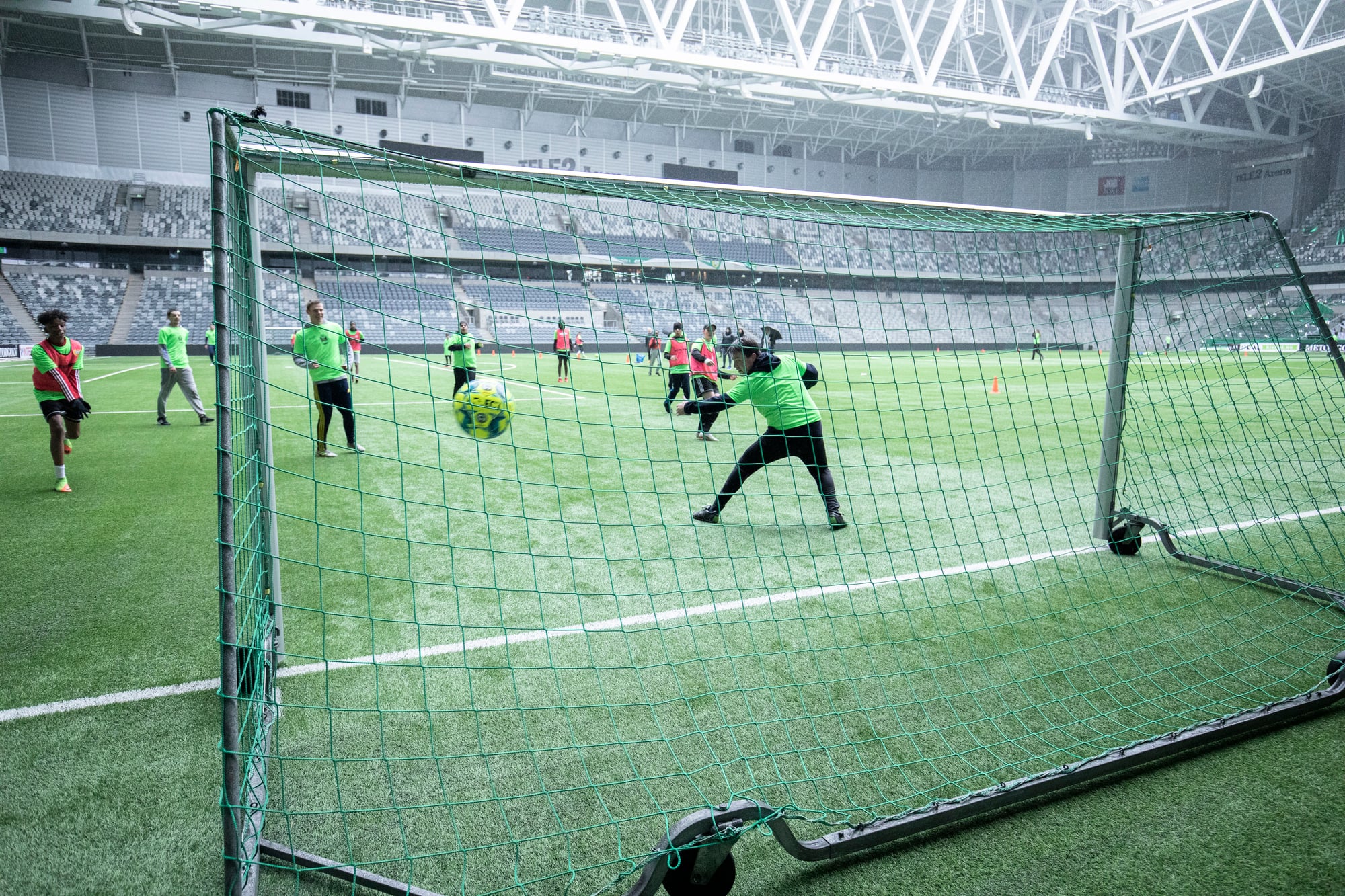 Baksidan av ett fotbollsmål där man ser hur ett gäng spelar fotboll och bollen är på väg in i mål. 
