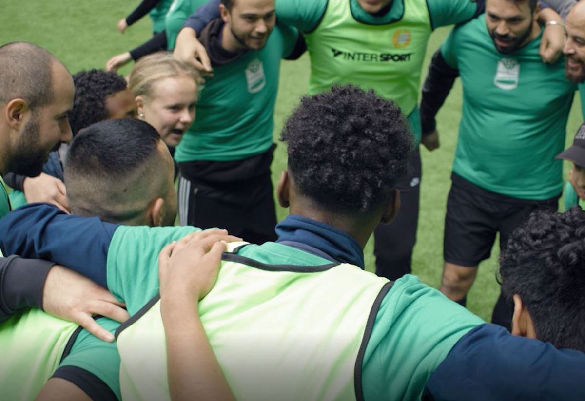 Ett gäng blandade unga och vuxna står och håller om och peppar varandra i en ring inför en match.