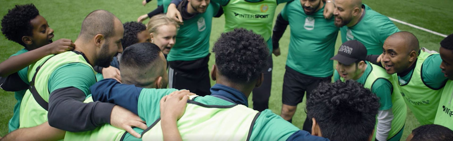 Ett gäng blandade unga och vuxna står och håller om och peppar varandra i en ring inför en match.