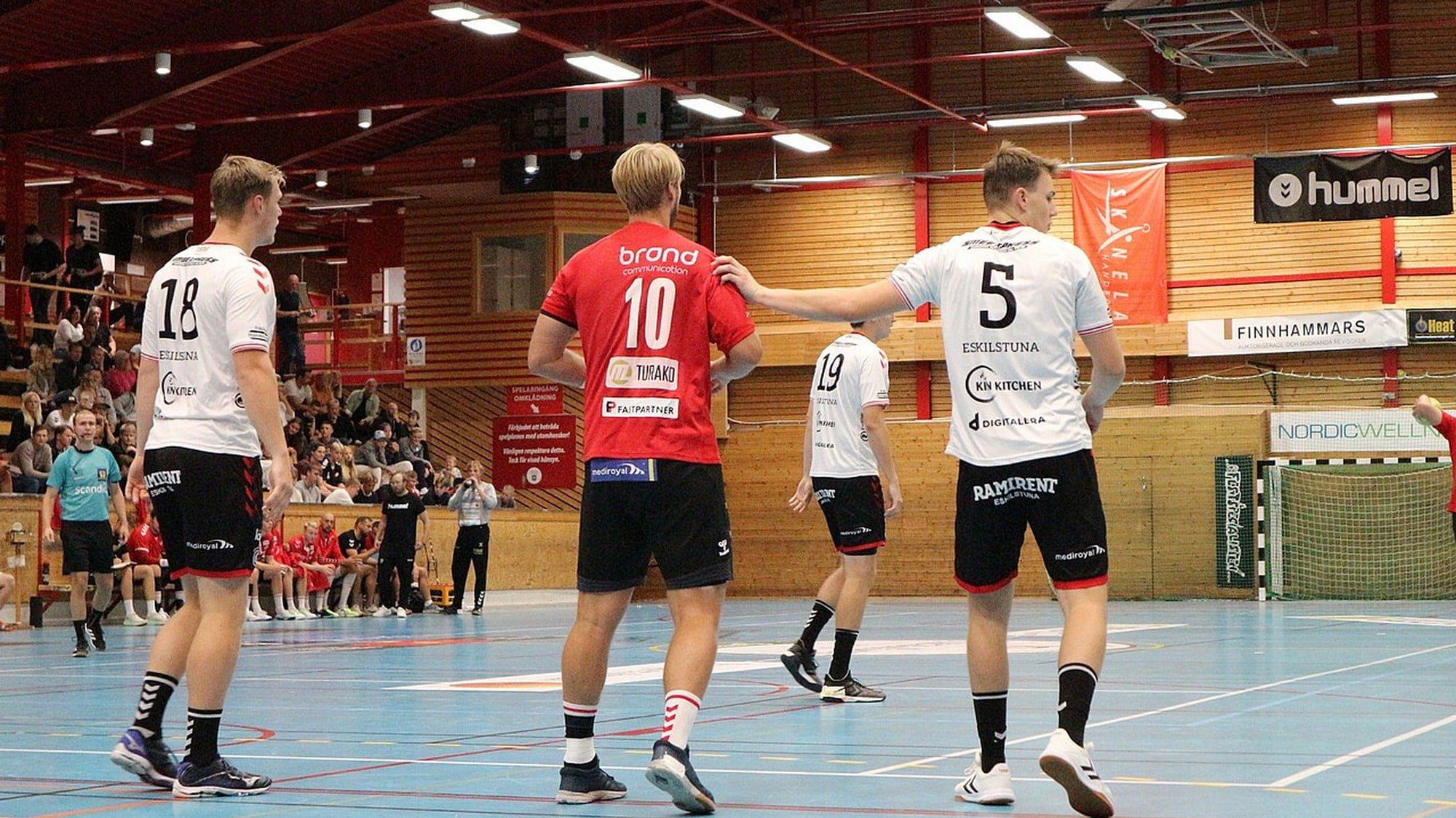 Bild från handbollsplan med spelare från ett rött och vitt lag.