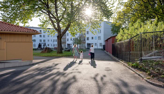 Bilden visar en familj som går i ett soligt bostadsområde, tillhörande Stena Fastigheter, i Tynnered i Göteborg