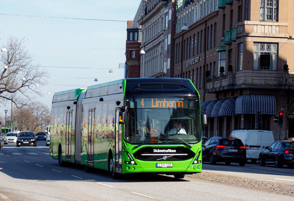 En grön stadsbuss från Skånetrafiken kör längs en stadsgata i Malmö med destinationen "Limhamn" visad på displayen. Bussen har linjenummer 4 och är omgiven av andra fordon och klassiska byggnader med butiker och kontor. Det är dagtid och vädret är klart.