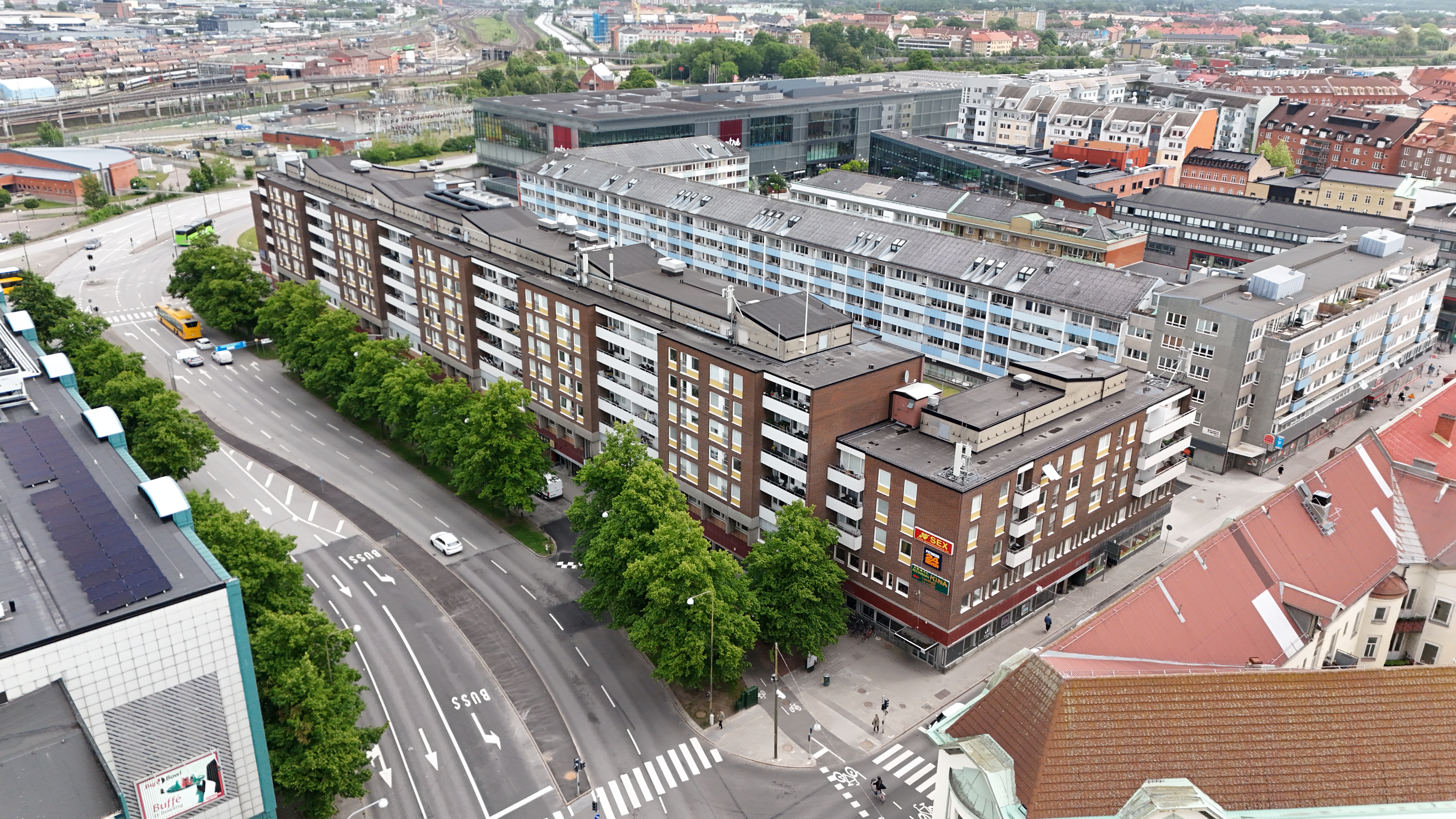 Flygbild över ett stadskvarter med flerbostadshus längs en trädkantad gata, där en röd markering visar en byggnad i området.