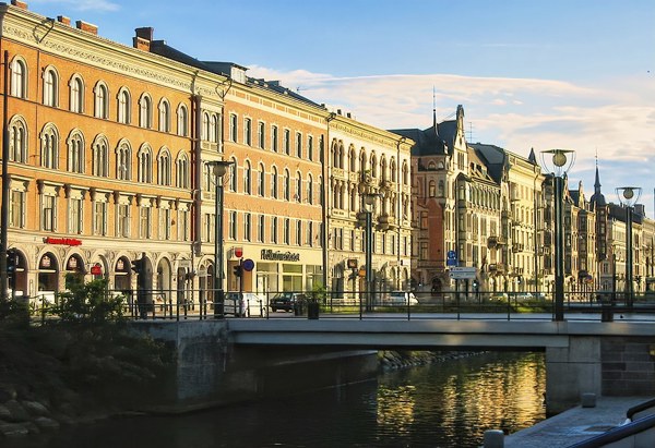 Klassiska byggnader längs en kanal med en bro i förgrunden, belysta av kvällssol under en klar himmel.