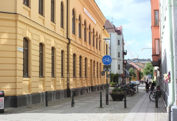 En gata med gula byggnader och cyklar parkerade längs trottoaren, under en delvis molnig himmel.