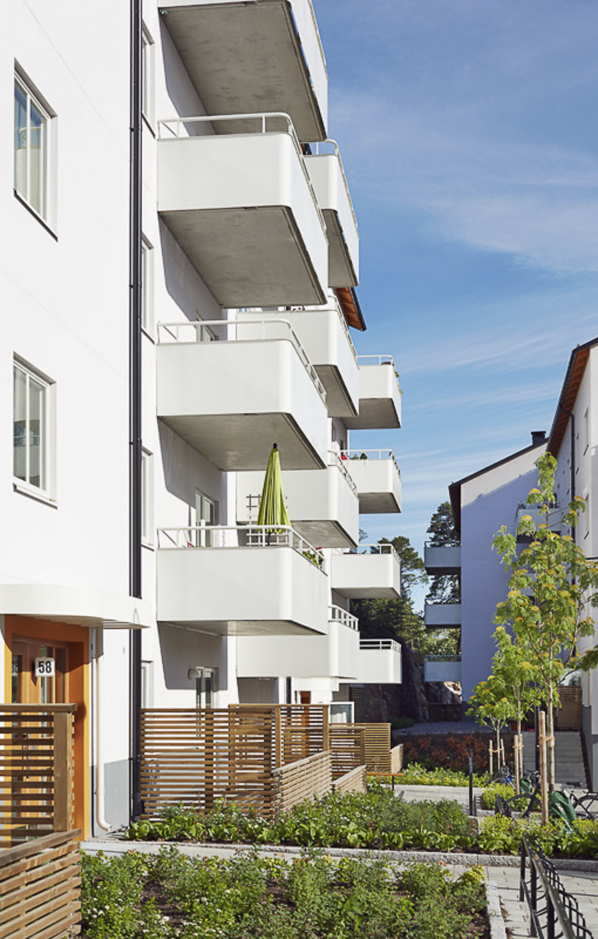 Modernt flerbostadshus med vita fasader, balkonger och grönskande innergård.