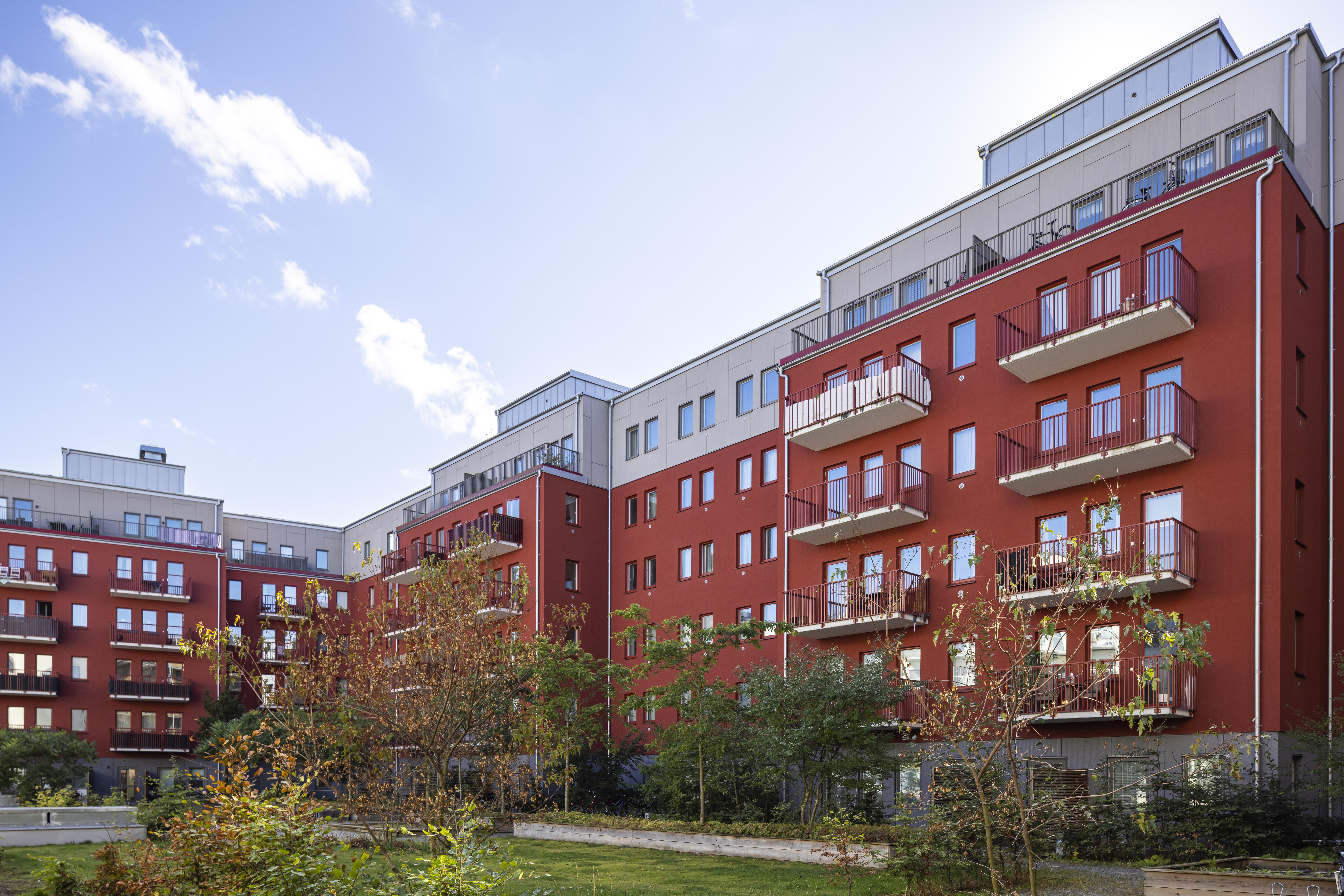 Flerbostadshus i Barkarby med röda fasader, balkonger och grönskande gårdsmiljö.