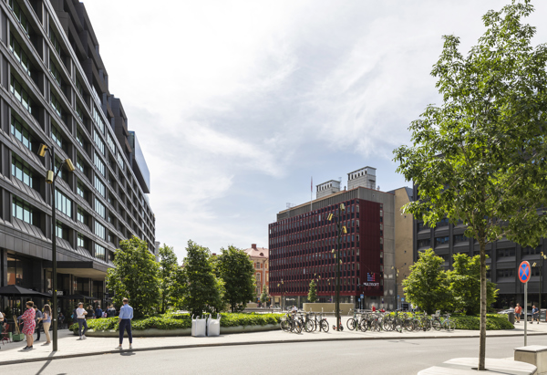 Foto på ett torg med höga hus runt om och några träd i förgrunden.