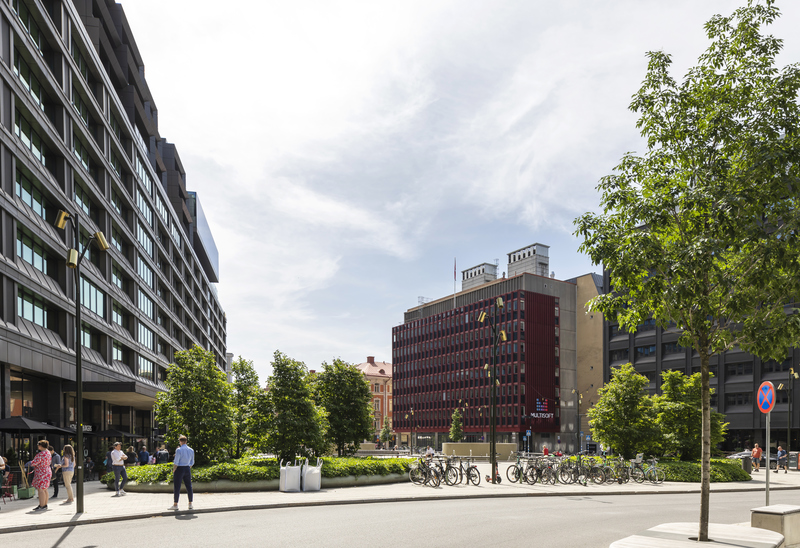 Foto på ett torg med höga hus runt om och några träd i förgrunden.