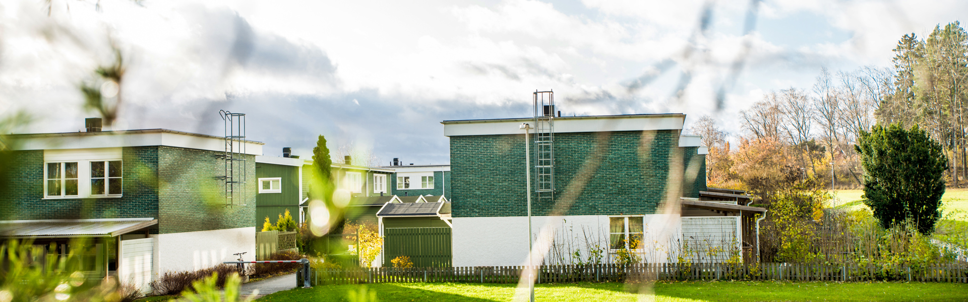 Radhus med en vit panel och grönt tegel i Ekebo, grenar och grönska i förgrunden.