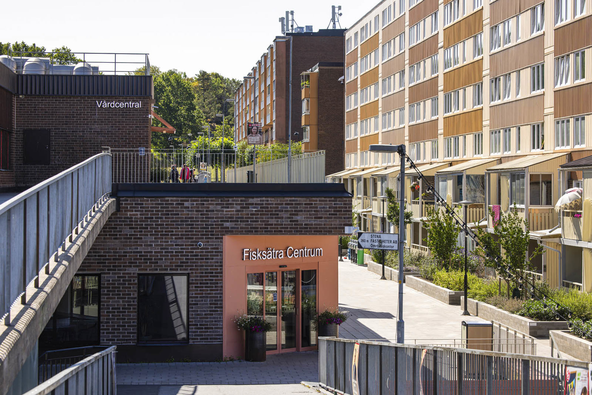 Orangea flerfamiljsbyggnader med en lägre tegelbyggnad i fokus som har skylten Fisksätra Centrum