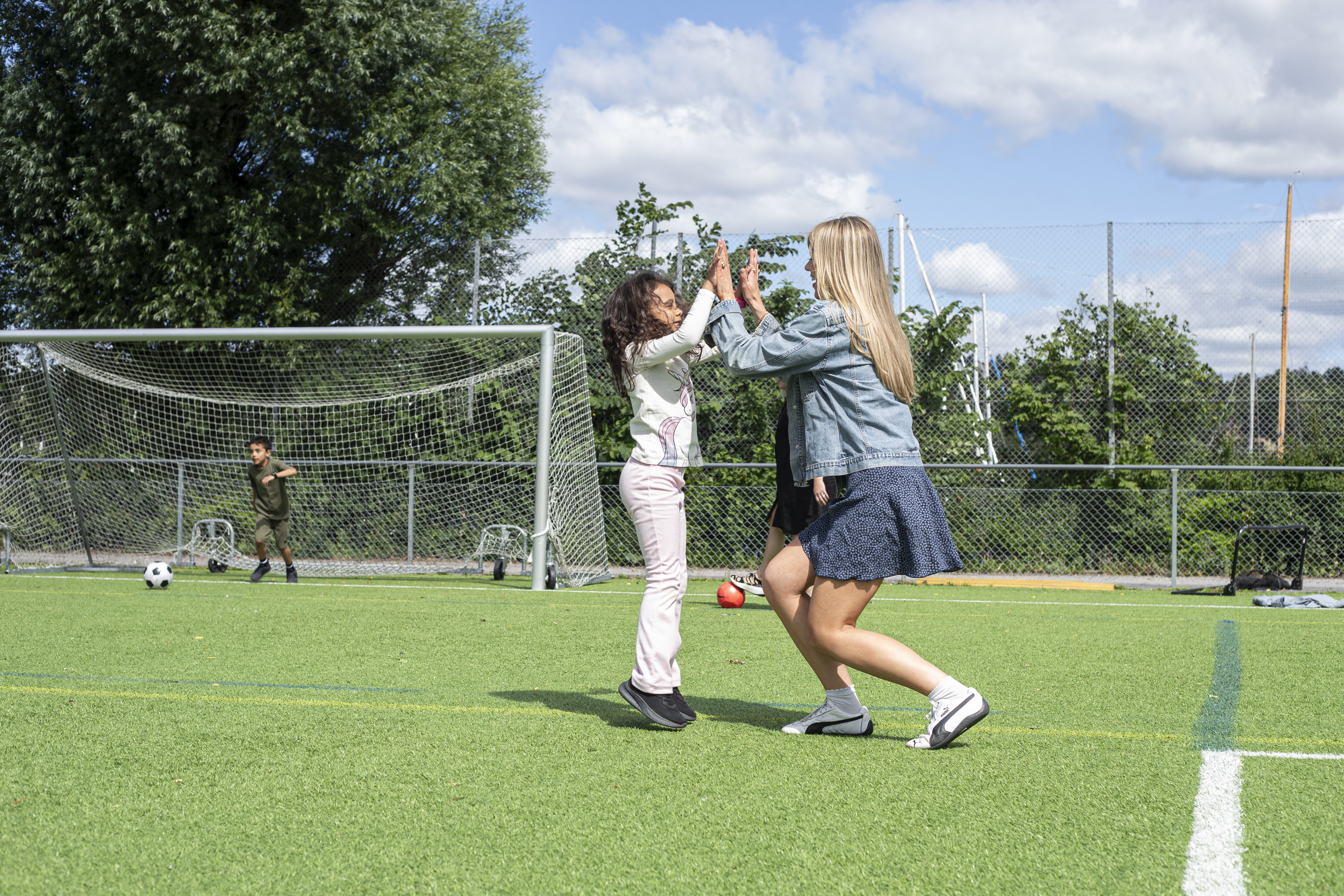 en fotbollsplan med en tjej och ett barn som gör high five en somrig dag