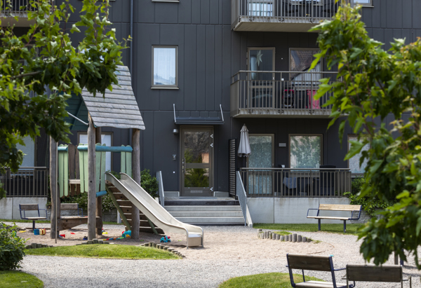 En lekplats i grönska med ett grått hus i bakgrunden. 