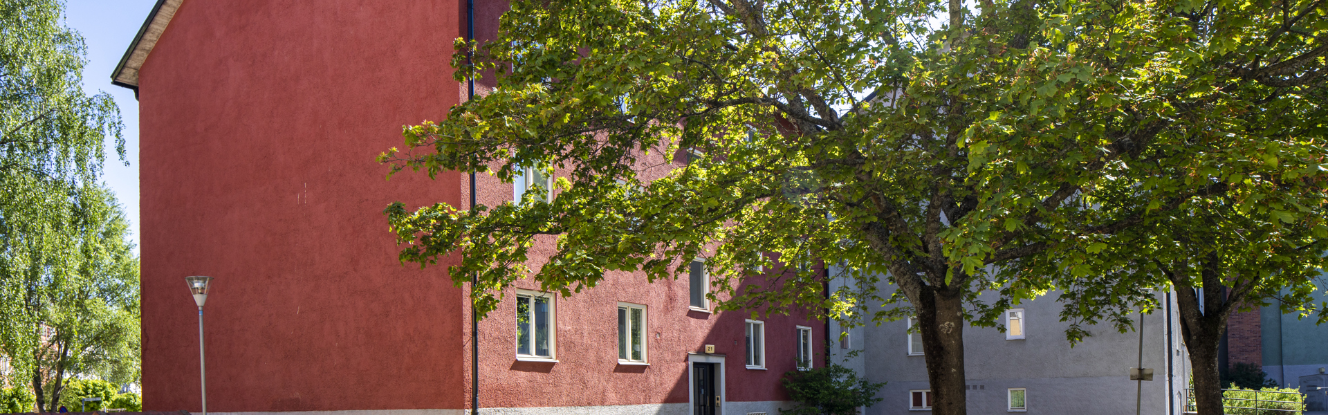 Rött hus i sommarmiljö med grönskande träd framför.