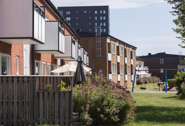 Flerfamiljshus i tegel med en uteplats och en stor buske, fler hus i bakgrunden.