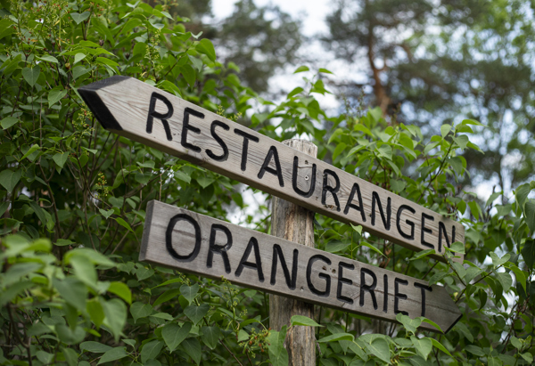 Skyltar i skogen som visar vägen. På skylten står det Restaurangen Orangeriet.