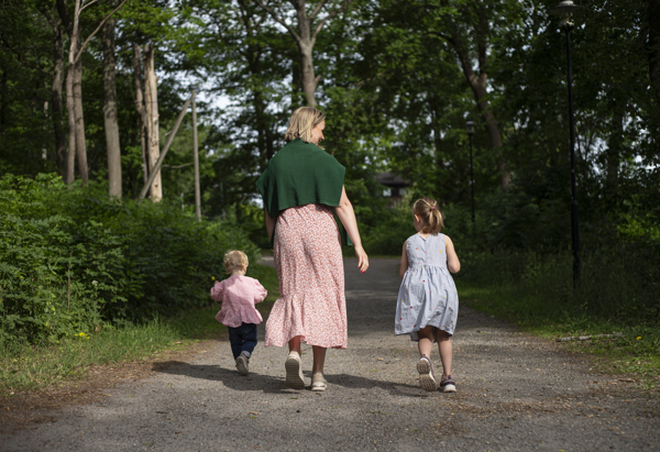Vuxen med två barn som springer på en stig i skogen på sommaren.