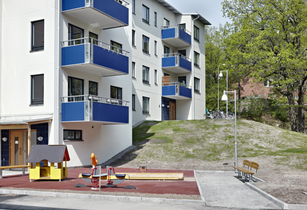 Vitt flerfamiljshus med blå balkonger och en lekplats.