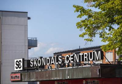 Sköndals centrums skylt på tak i fokus med hus i bakgrund