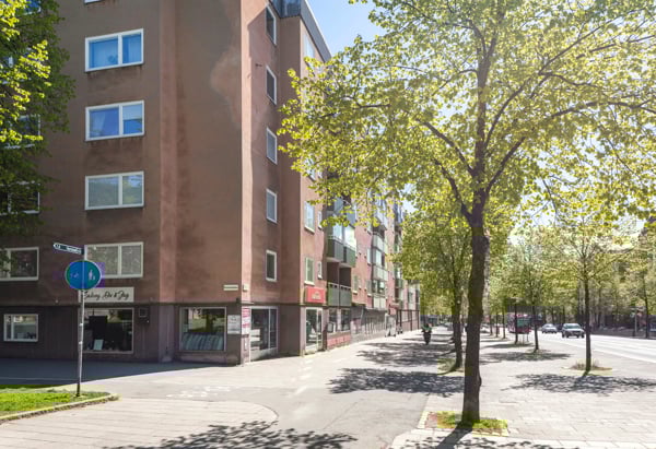 En gata med ett rött flerfamiljshus och grönskande träd.