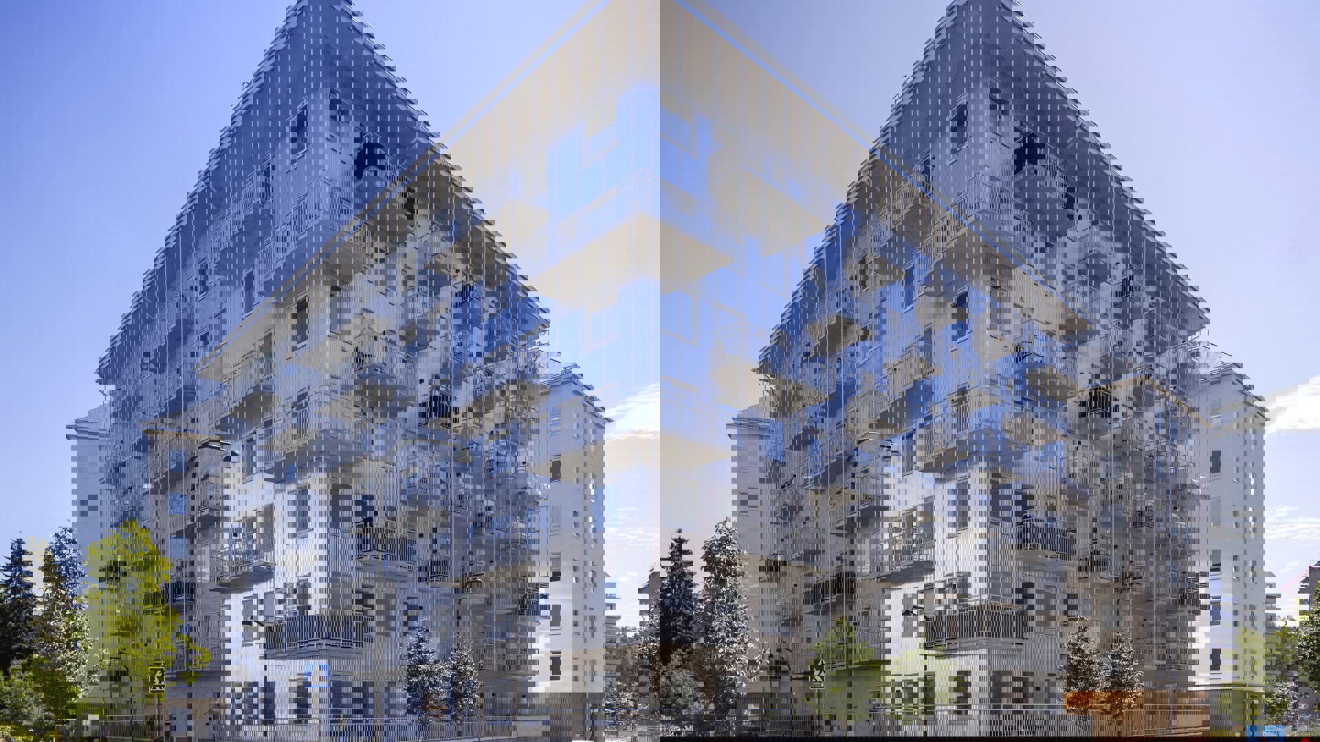 Flerbostadshus i modern stil med fasad i silverfärgad plåt och många utskjutande balkonger, sett från gatan en solig dag med blå himmel, trädplanteringar längs trottoaren och parkerade bilar framför huset. Supernova i Vega Haninge