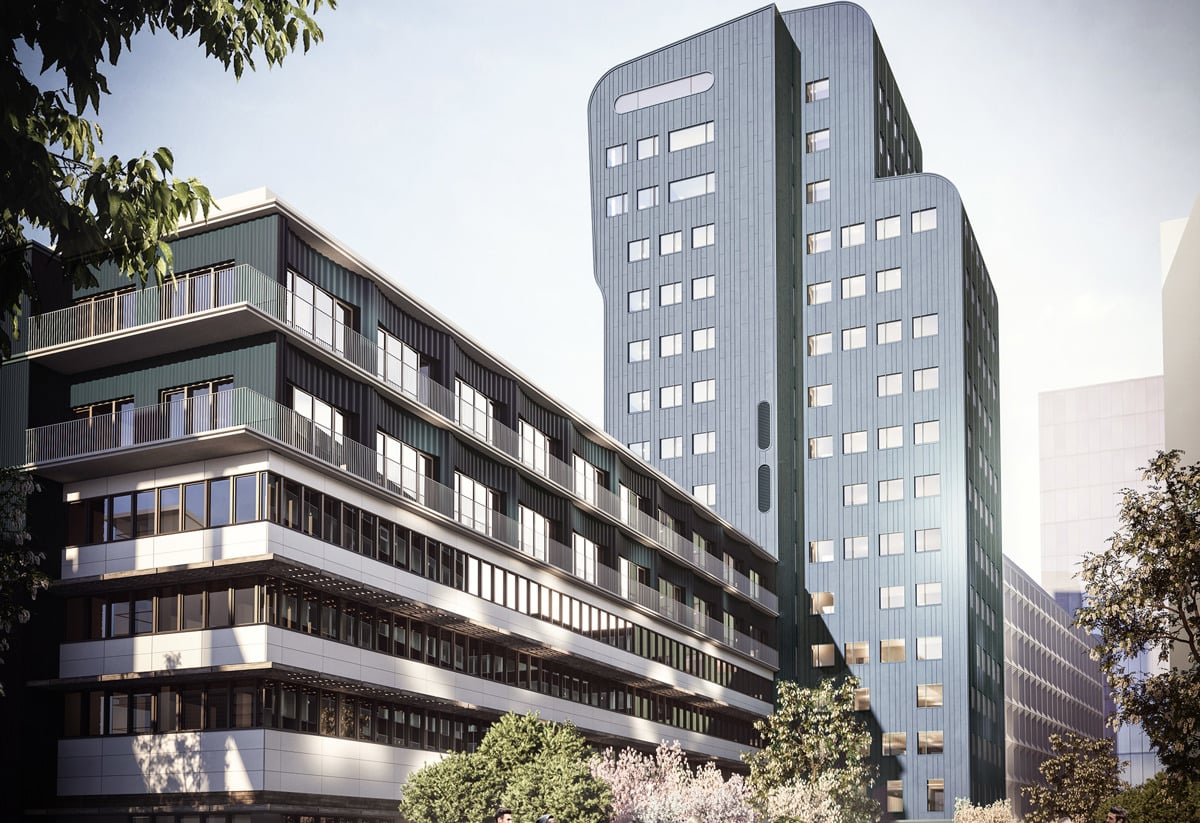 En modern byggnad med en hög, blå fasad och lägre sektioner med balkonger. Människor promenerar och cyklar på en bred gångväg omgiven av träd och buskar. Himlen är ljus och klar.