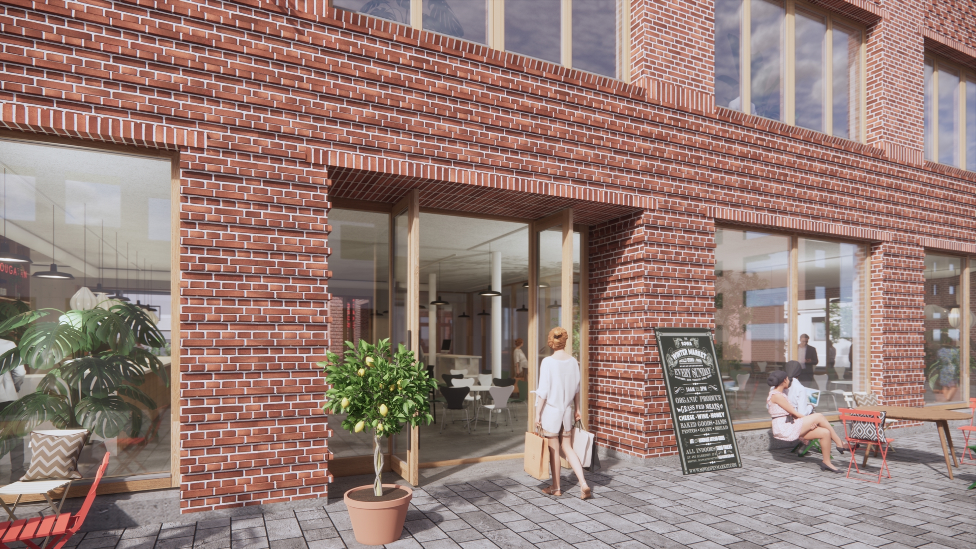  En tegelklädd husfasad med stora glasdörrar in mot ett ljust café eller kontorsrum. En person går in genom entrén, medan en annan sitter vid ett bord utomhus. Framför dörren står en kruka med ett citronträd och en svart meny- eller informationsskylt, samt några utemöbler på den stenlagda trottoaren.