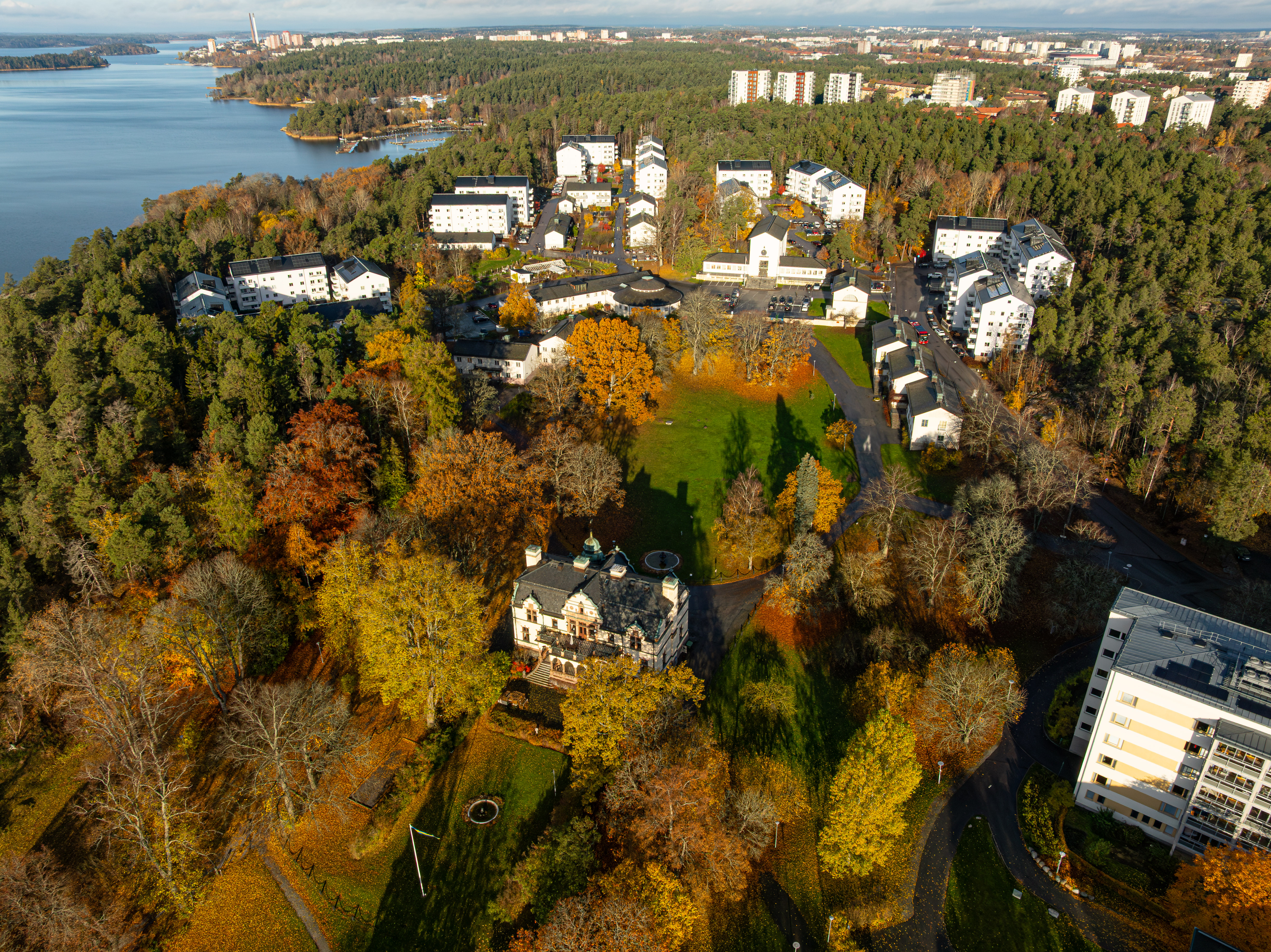Flygbild över Ängby Park med slottet närmast och de vita flerfamiljshusen i bkagrund. Omgiven av vatten och grönska