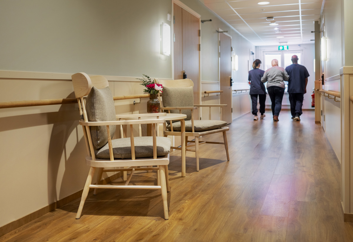 Bild från äldreboende där två i personalen går arm i arm med en boende