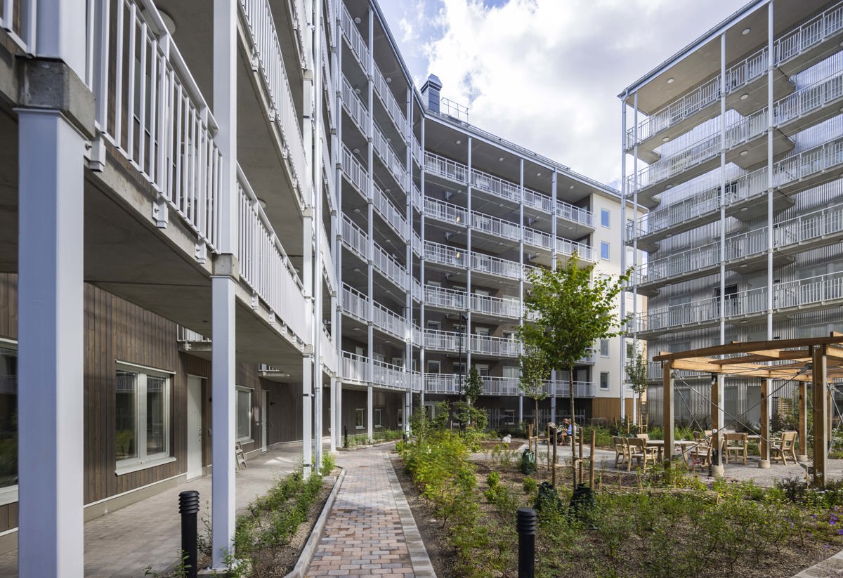 Lummig innergård med en gångväg genom grönskan som omsluts av vita lägenhetshus.