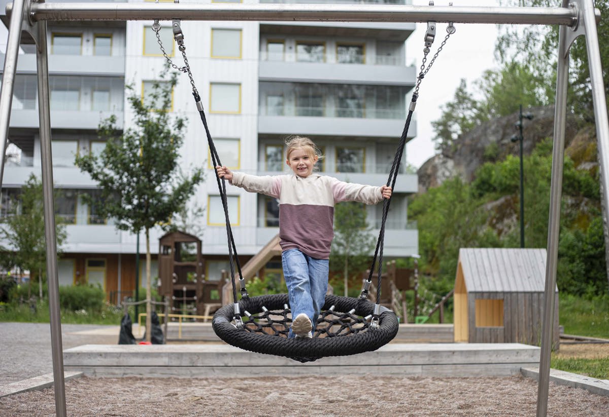 Flicka som gungar i en lekpark i Vega med hus i bakgrunden